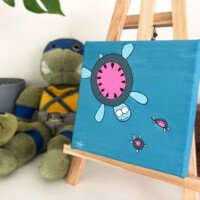 Bright cartoon painting of a large pink-shelled turtle with two smaller turtles on a blue background, displayed on a wooden easel.